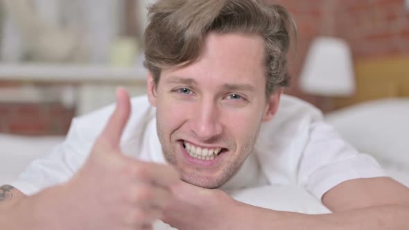 Cheerful Young Man Showing Thumbs Up in Bed
