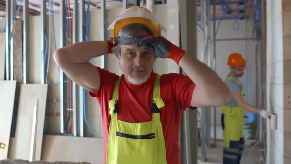 Mature Builder Putting on Plastic Face Mask on Construction Site