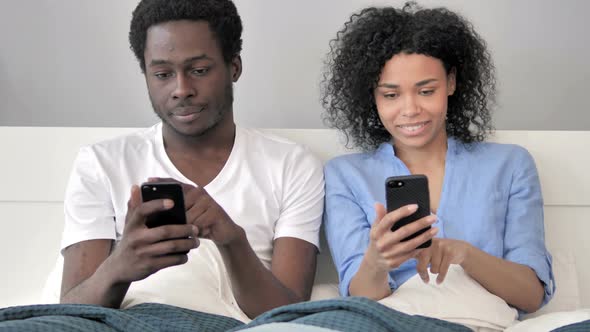 African Couple Using Smartphone in Bed