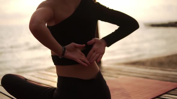 Woman Practicing Yoga and Stretching Spine and Hands Sitting on Mat on Sea Pier Joins Hands Behind