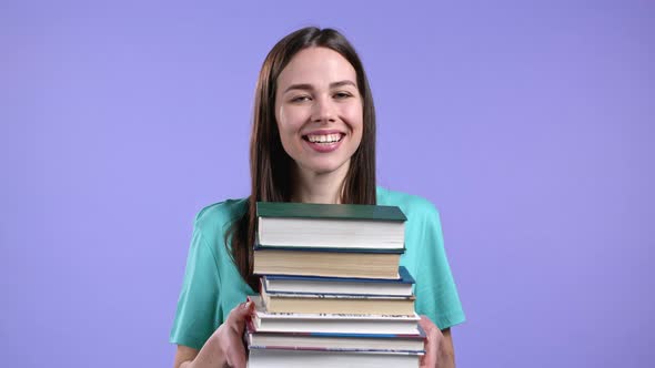 Student Holds Stack of University Books From Library on Violet Background in Studio