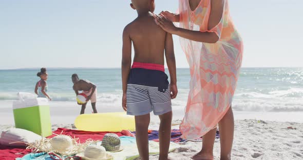 Smiling african american family using sun cream on sunny beach