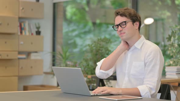 Young Man Having Neck Pain While Using Laptop in Modern Office