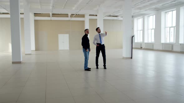 Realtor and Businessman Stand in Middle of an Empty Room and Inspect It Front View