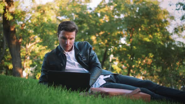 Young Handsome Man Using Laptop Laying on Grass in Park