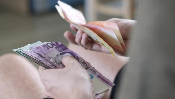 Men's Hands Count Cash Philippine Pesos and Other Currencies at Home in a Bright Room