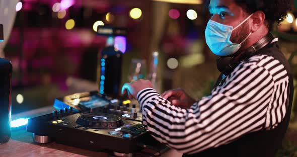 Dj mixing outdoor at cocktail bar - African young man mixing music while wearing safety mask