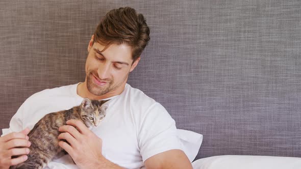 Young man sitting on bed stroking his tabby cat 4K 4k