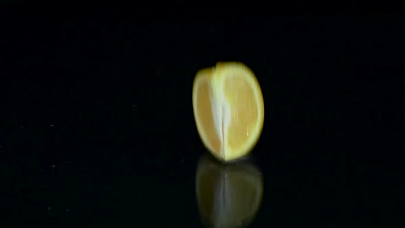 Quarter of Orange Falls Into the Water. Black Background. Slow Motion