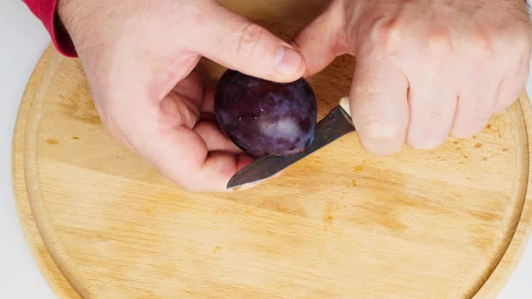 A man clumsily cuts large juicy plums in half with a knife. Very large dark blue plums