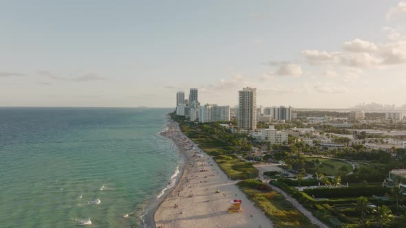 Aerial trucking of people relaxing in sand shore near turquoise sea in Miami Beach, resorts and apar