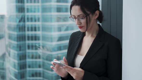 Portrait of a Young Businesswoman with a Mobile Phone in Her Hands. the Girl Is Intently Using a