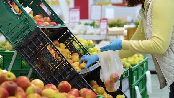 Shopper in medical gloves picking apples from plastic boxes at grocery store