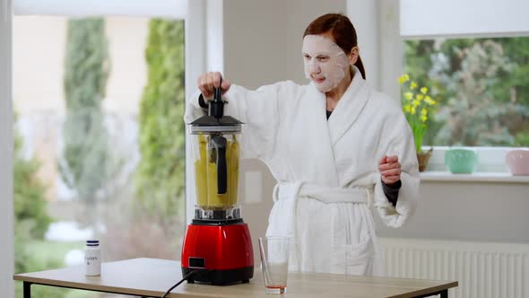 Positive Redhead Mature Woman in White Bathrobe and Facial Moisturizing Mask Mixing Ingredients in