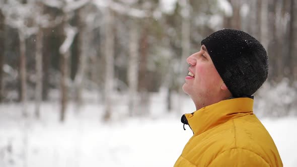 A Man in a Yellow Jacket Looks at the Snow in the Winter in the Woods and Smiles in Slow Motion