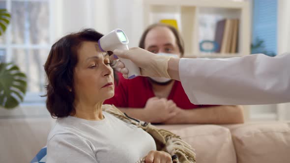 Young Man in Safety Mask Watching Doctor Measuring Temperature of Sick Aged Mother