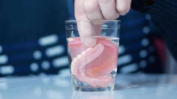 Close-up. An elderly man takes dentures from a glass of water. false teeth in old age