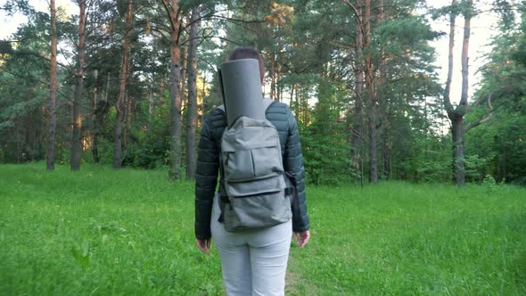 Young Woman with a Backpack Walks Through the Woods Alone