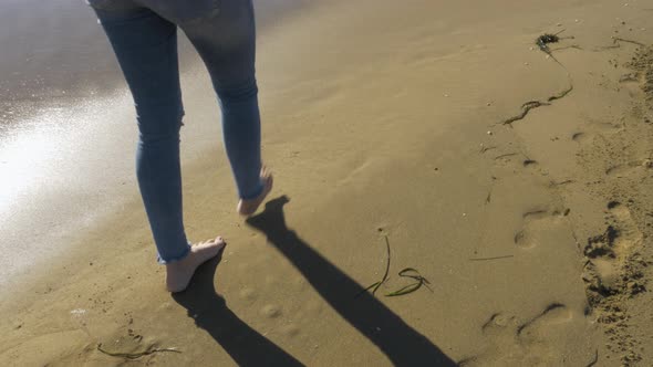 Female legs walk along a beach and leave footprints behind.