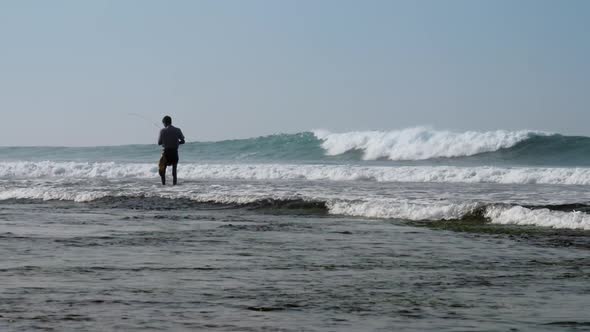 Local Fisherman Holds Rod in Hand in Waving Blue Ocean