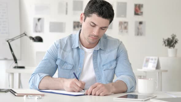 Casual Young Man Writing in Office