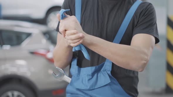 Unrecognizable Auto Mechanic in Uniform Rubbing Hands with Cloth Indoors