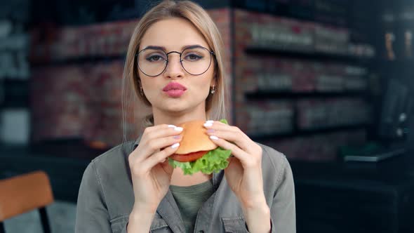 Pleasant Woman Biting Desired Fresh Hamburger Admiring Amazing Taste Looking at Camera