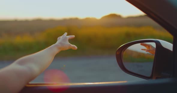 A Young Girl Put Her Hand Out of the Car Window at Sunset