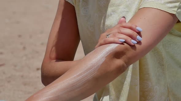 Woman Spreading Sunscreen on Her Arm at the Beach on a Hot Sunny Day