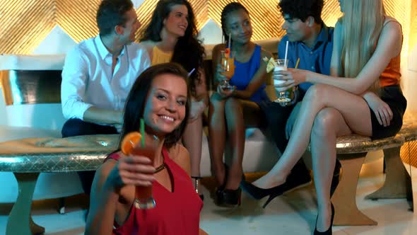 Portrait of woman holding a cocktail while friends sitting behind
