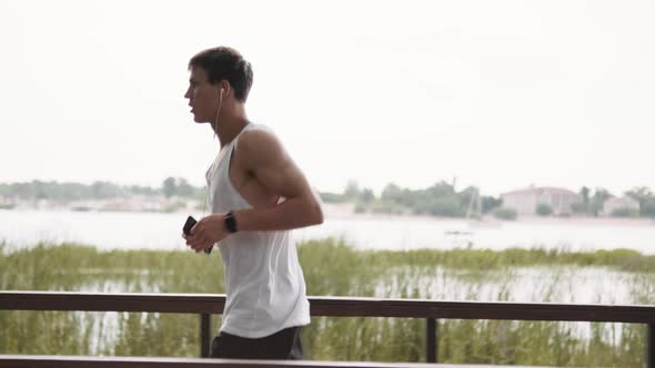 A side view of a muscular guy is running while listening music