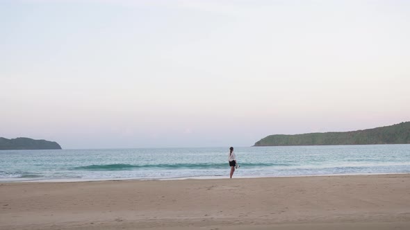 Young woman walking barefoot in the sand in the distance at dusk on Nacpan Beach, Palawan, the Phili