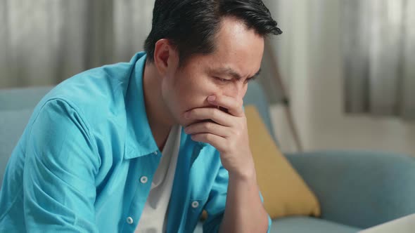 Close Up Of Asian Man Being Worried While Typing On A Laptop At Home