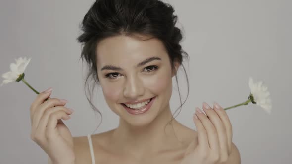 Young and Beautiful Woman with Lovely Smile Hiding Eyes Behind Camomile Flowers and Laughing