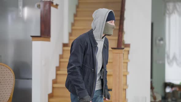 Masked Suspicious Young Thief Standing in Rich House and Suddenly Looking at Camera