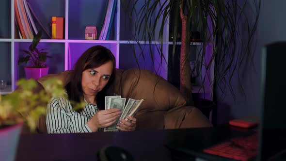 Young Woman Counts Money Sitting in Armchair Before Computer in Office