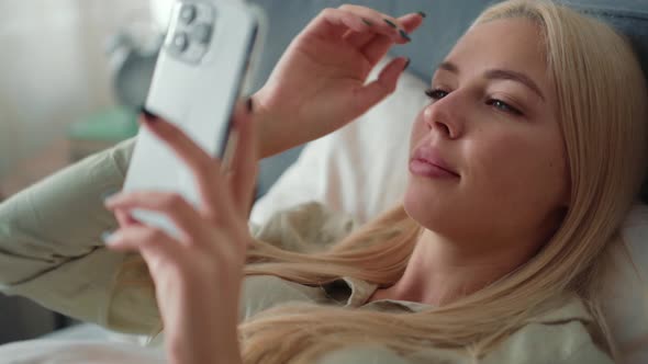 Handsome blond woman texting by phone in bed