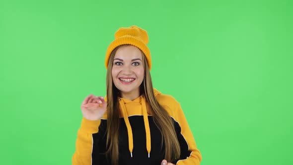 Portrait of Modern Girl in Yellow Hat Is Waving Hand and Showing Gesture Come Here. Green Screen