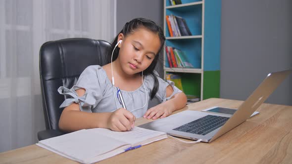 Asian Little Girl Writing And Use Laptop At Home