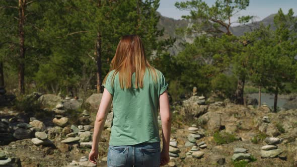 Woman Walks to Stacked Stones Near Pine Forest at Altai