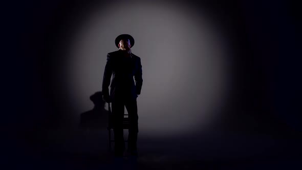 Elegant Man in a Black Hat Is Dancing an Erotic Dance. Spotlight on a Black Background.