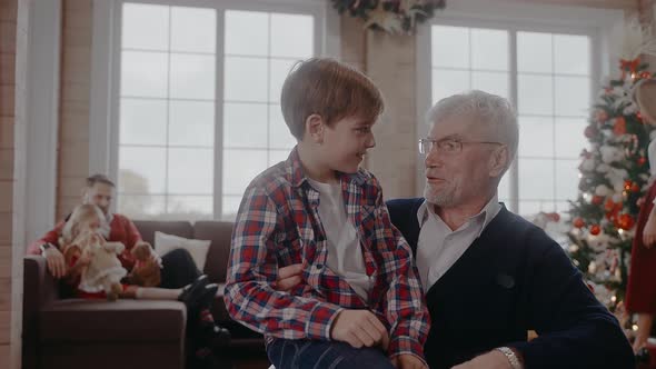 Boy Sitting on a Chair with His Grandad and Talking at Christmas Celebration