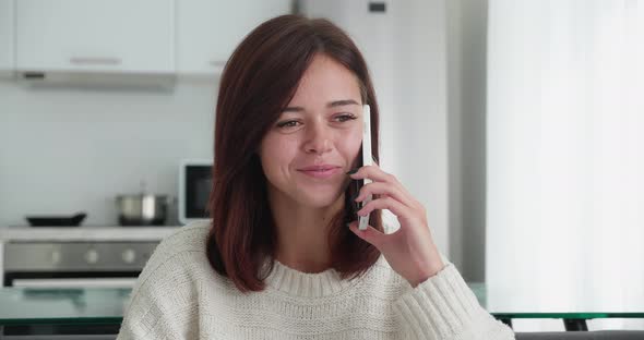 Smiled Caucasian Young Woman Speaking on the Mobile Phone While Sitting on Cozy Sofa in the Living