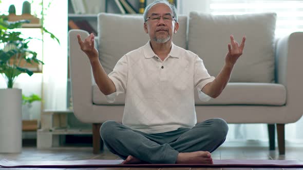 Asian elderly senior man doing yoga for meditation on yoga mat in living room