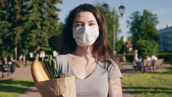 Caucasian Young Pretty Woman Delivery Worker in Medical Mask Walking the Street and Carrying Packet