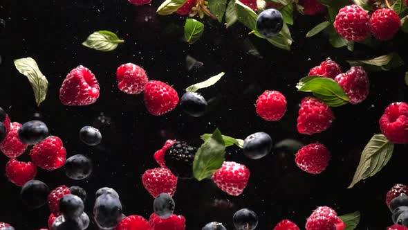 Fresh Raspberries with Blueberries and Fresh Mint Leaves Fall on a Black Background Into the Water