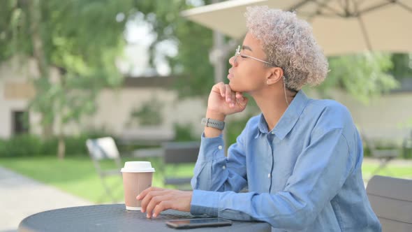 Young African Woman with Coffee Thinking in Outdoor Cafe