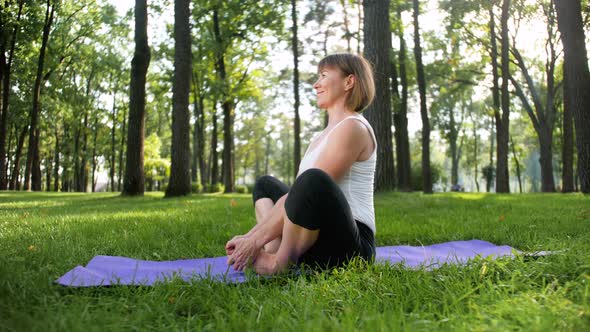 Happy Smiling Woman Stretching on Fitness Mat at Park. Middle Aged Lady Doing Yoga