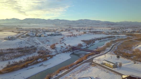 Aerial view of a neighborhood with children sledding down a slope near a river and bridge with mount