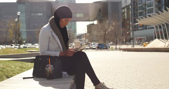 Side view of young Asian woman in hijab using digital tablet in the city 4k